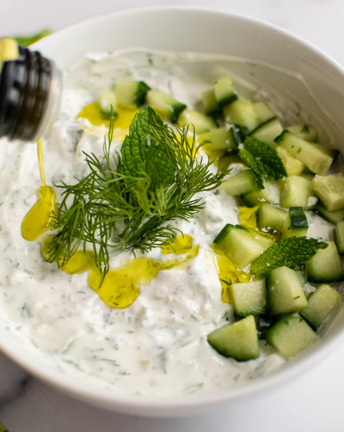 Drizzling olive oil over tzatziki