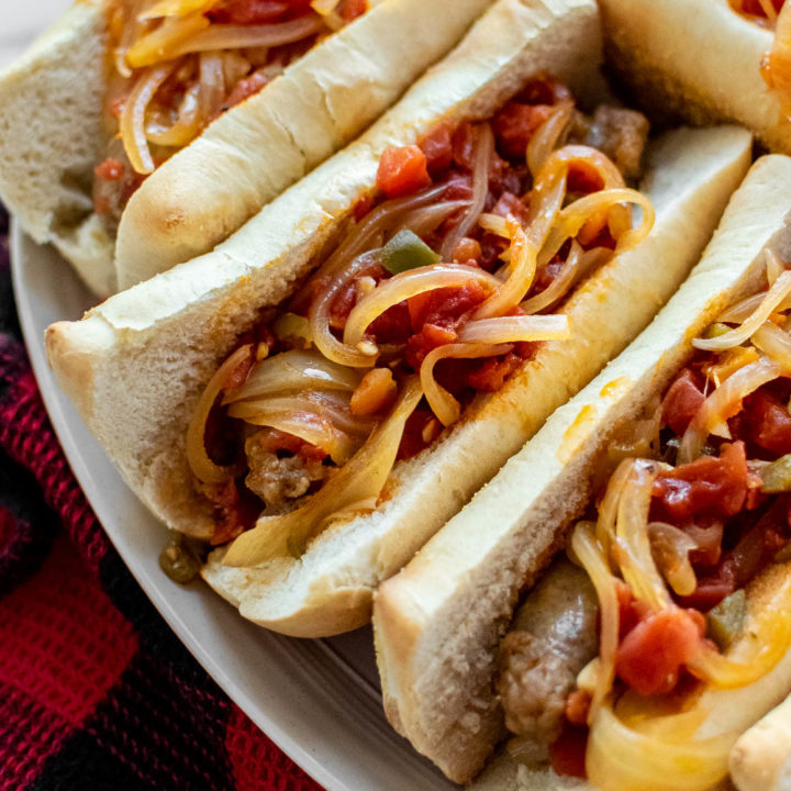 Italian Sausages With Spicy Tomato Sauce And Onions in buns on a serving platter.