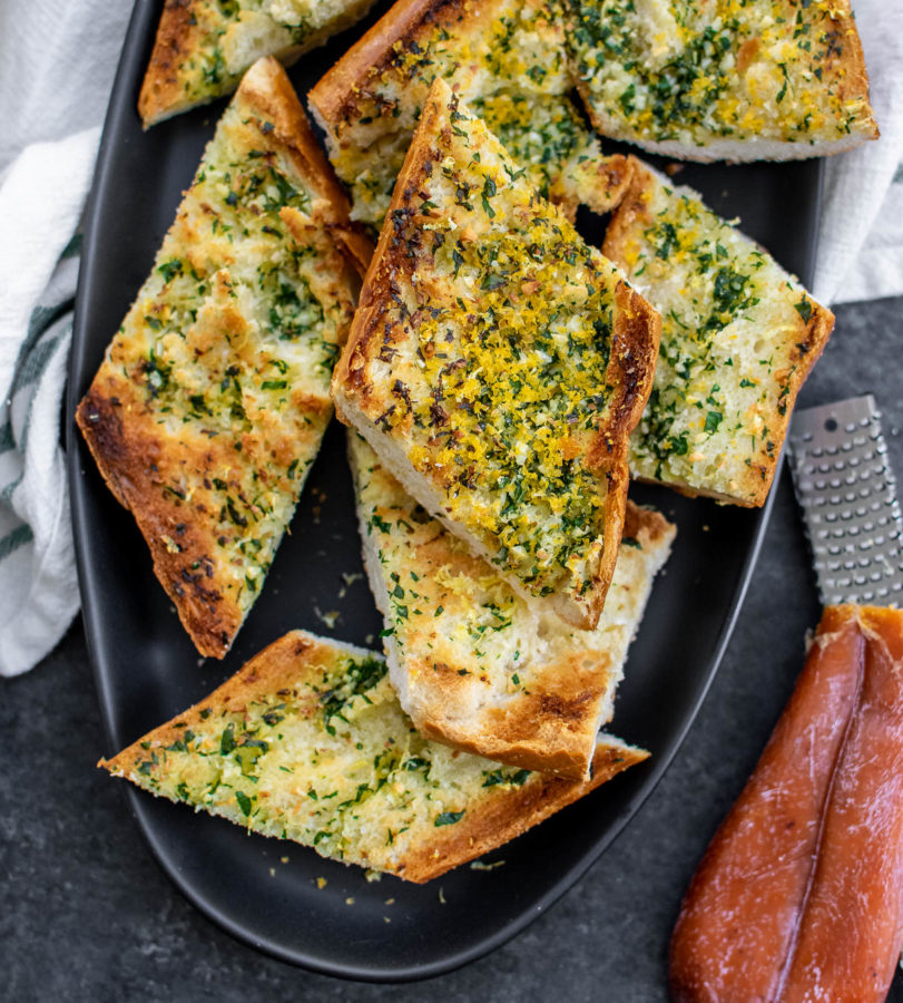 Garlic Bread with Bottarga on a platter with bottarga and microplane next to it.