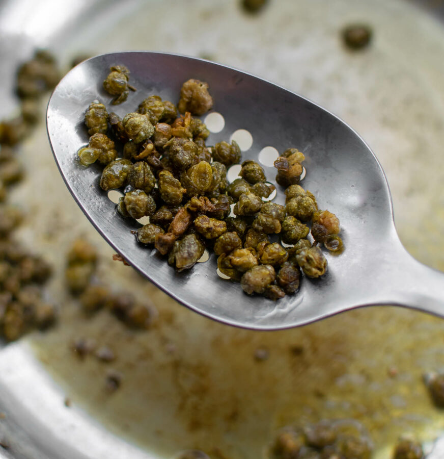 Fried Capers being scooped from the pan with a slotted spoon.