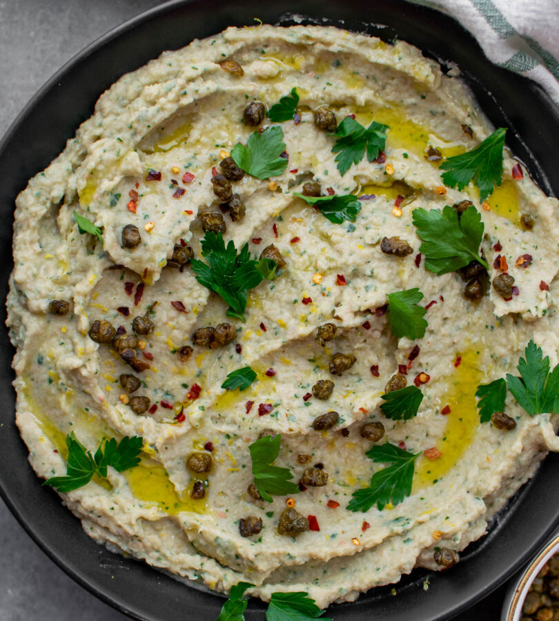 Roasted Garlic and Artichoke White Bean Dip with Fried Capers in a bowl.