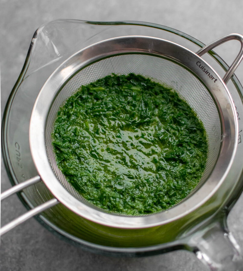 Chive oil being strained through a fine mesh strainer.