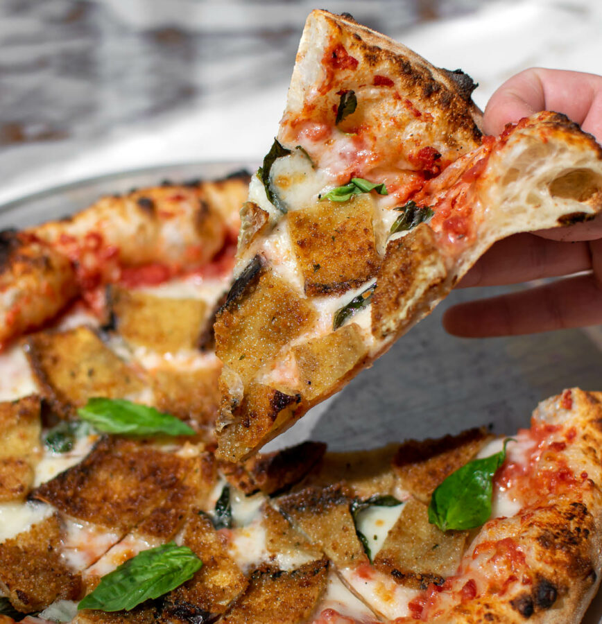 Fried Eggplant Parmesan Pizza slice being picked up.