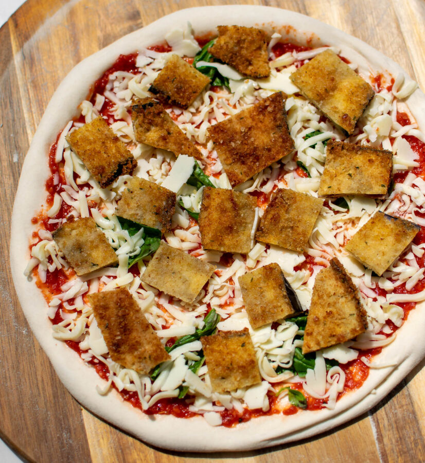 Fried Eggplant Parmesan Pizza on a pizza peel, before baking.