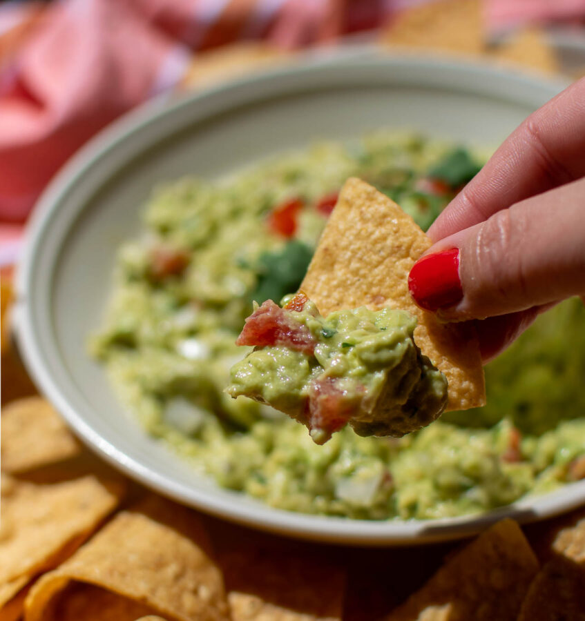Easy Authentic Guacamole being scooped from a bowl with a tortilla chip.